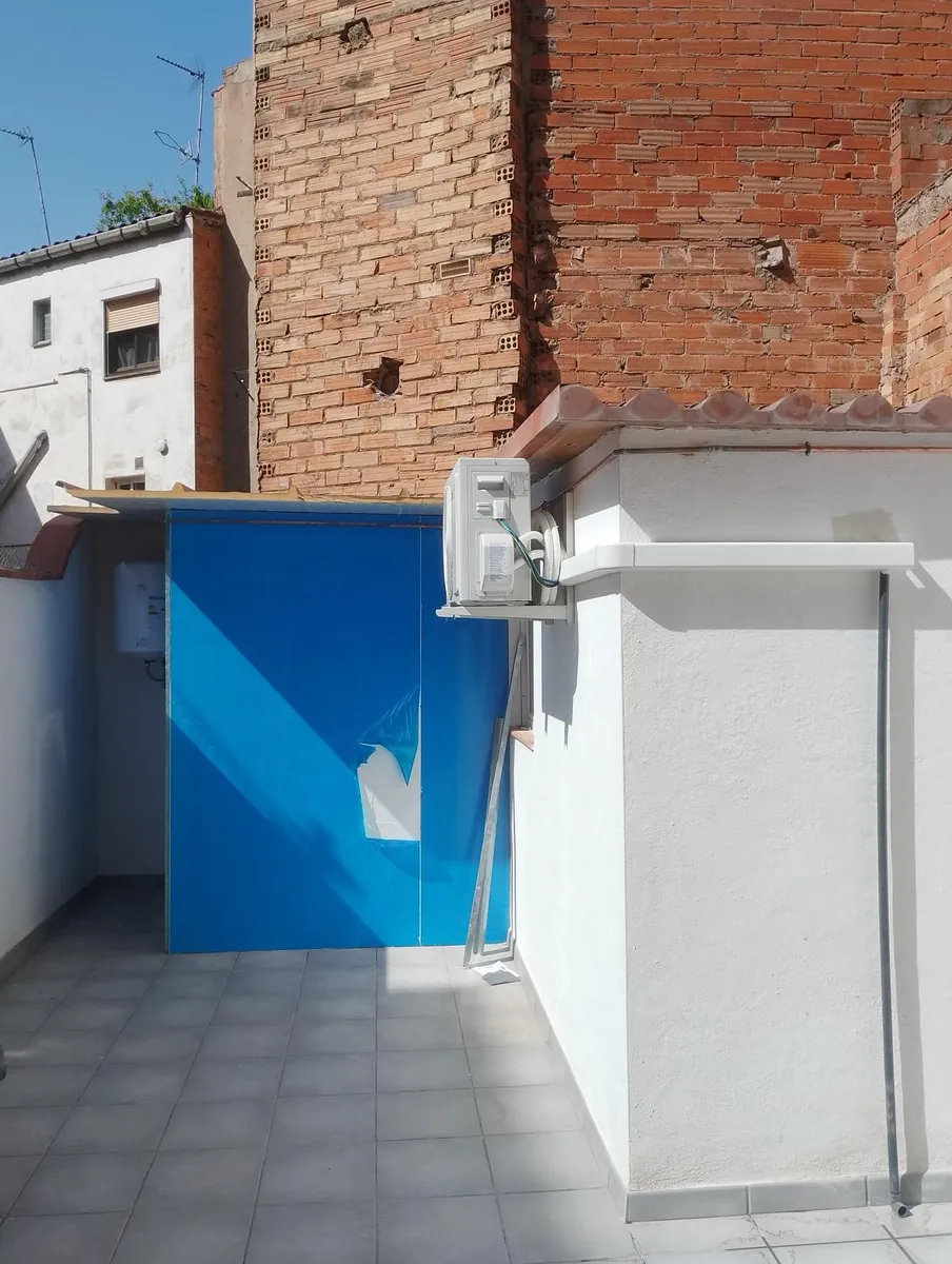 Unidad exterior de aire acondicionado sobre soporte de pared en una terraza reformada