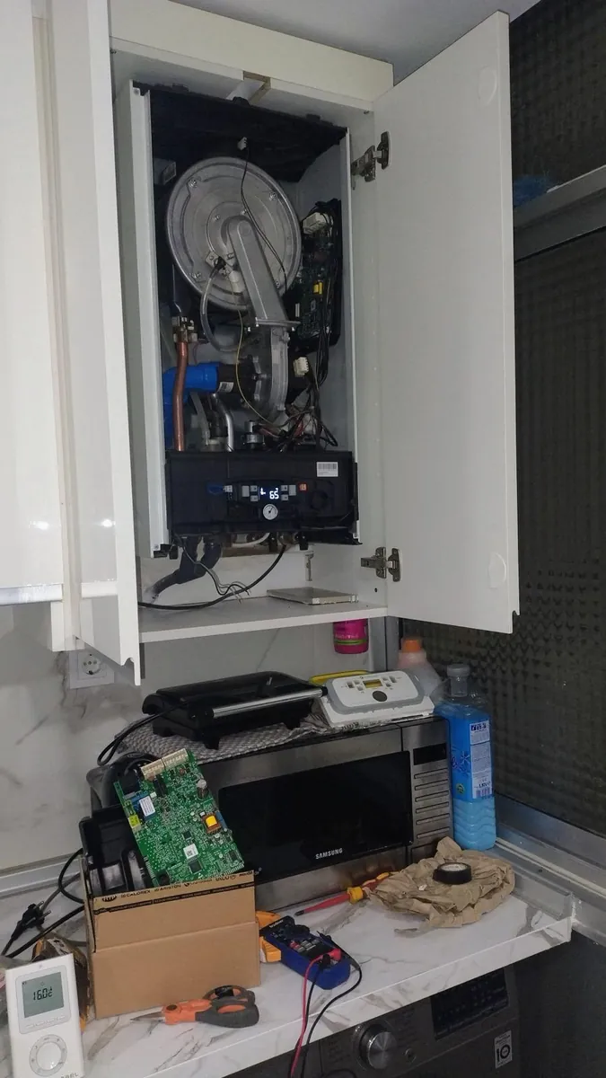 Caldera abierta en armario de cocina con la placa electrónica nueva y el polímetro sobre la encimera